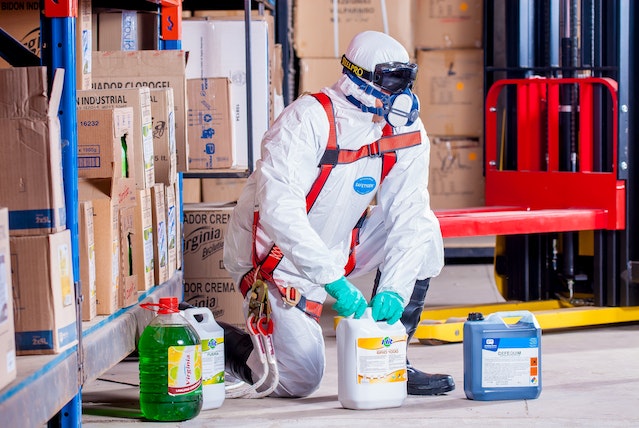 a person in a white protective suit, handling with multiple chemical products.